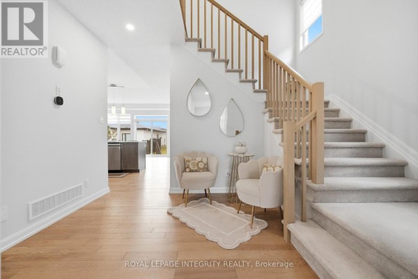 Foyer with a light wood staircase, two cream armchairs, and a view into the kitchen and backyard. - 441 Sterling Avenue, Clarence Rockland