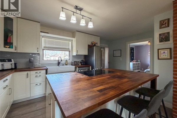 View of the kitchen's white cabinets, farmhouse sink, and butcher block island with seating. - 442 Front Street W, Eastend