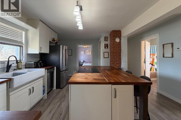 Kitchen with light blue walls, white cabinets, a butcher block island, and views into adjacent rooms. - 442 Front Street W, Eastend