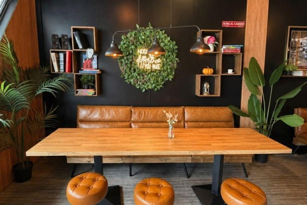 Seating area with a long wooden table, tan leather banquette, and upholstered stools against a black wall. - 442 Hazeldean Road, Ottawa