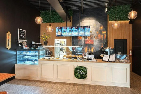Cafe counter with a glass display case of pastries, menu screens above, and artwork on the back wall. - 442 Hazeldean Road, Ottawa