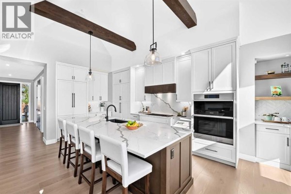 Modern white kitchen with a large island, dark wood cabinets, and stainless steel appliances. - 443 Grayling Lane, Rural Rocky View County
