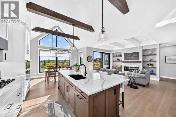 Open concept living and dining area with vaulted ceilings, exposed beams, and a fireplace. - 443 Grayling Lane, Rural Rocky View County