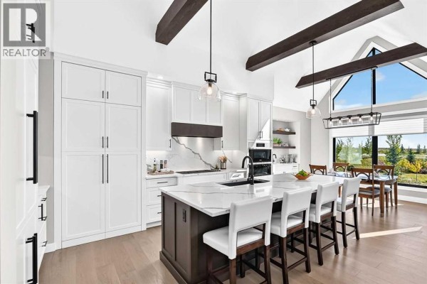 Spacious kitchen and dining area with white cabinets, an island, and large windows overlooking the countryside. - 443 Grayling Lane, Rural Rocky View County