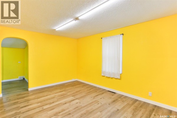 Bright yellow room with wood laminate flooring, a window, and an arched doorway. - 443 Lillooet Street W, Moose Jaw