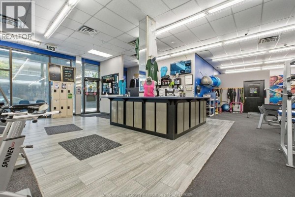 Interior view of a gym with a reception desk, exercise machines, and storage units. - 443 Ouellette Avenue, Windsor