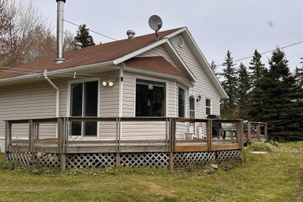 Rear view of a beige vinyl-sided house with a wrap-around wooden deck and outdoor furniture. - 4430 252 Highway, Hillsboro