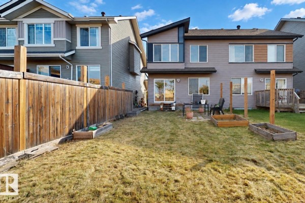 Backyard of a duplex with a wooden fence, grass, and raised garden beds. - 4434 Prowse Rd Sw, Edmonton