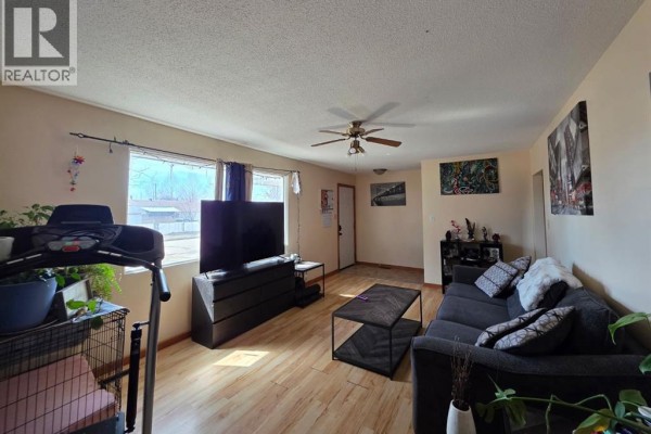 Living room with wood laminate flooring, large windows, a sofa, coffee table, and television. - 4436 51st Avenue, High Prairie