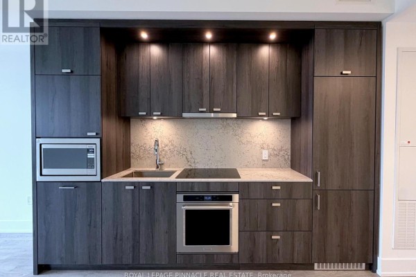 Close-up of a compact kitchen with dark wood cabinetry and stainless steel appliances. - 444 - 858 Dupont Street, Toronto