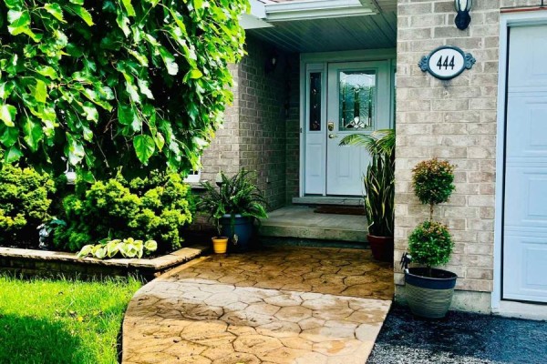 Close-up of the front door and porch area, featuring brick walls and potted plants. - 444 Bridge Street W, Greater Napanee