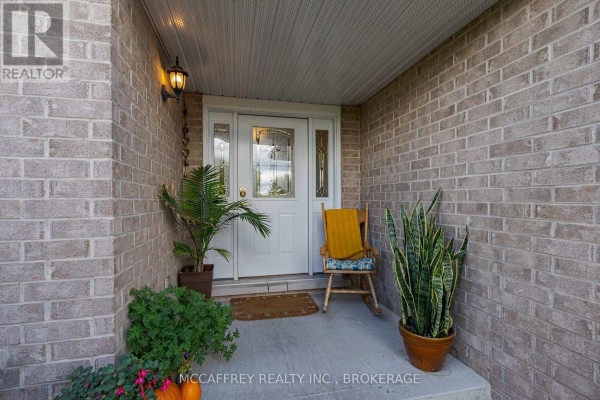 Covered porch with a white door, rocking chair, and potted plants beside brick walls. - 444 Bridge Street W, Greater Napanee