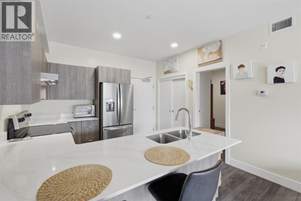 Kitchen island with sink, faucet, and seating for two with a view into the hallway. - 444 St Paul Street Unit# 507, Kamloops