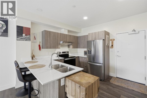 Corner kitchen with stainless steel appliances, island, and view of the apartment entrance. - 444 St Paul Street Unit# 507, Kamloops