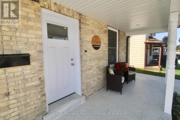 Close-up of the covered front porch of a yellow brick house with a white door and seating. - 445 11th Street, Hanover