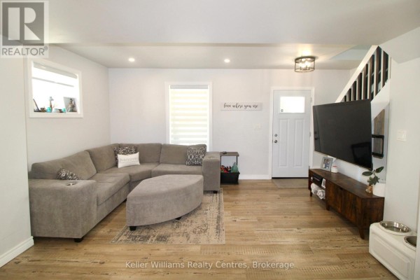 Living room with a sectional sofa, ottoman, large television, and wood-look flooring. - 445 11th Street, Hanover