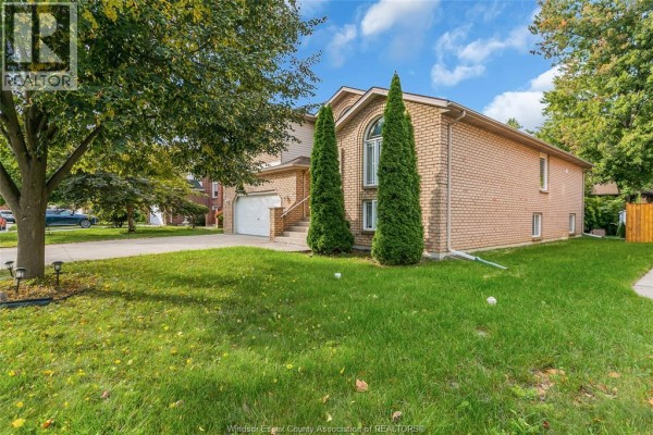 Side view of a brick house with a well-maintained lawn and mature trees. - 445 John Harvey Crescent, Windsor