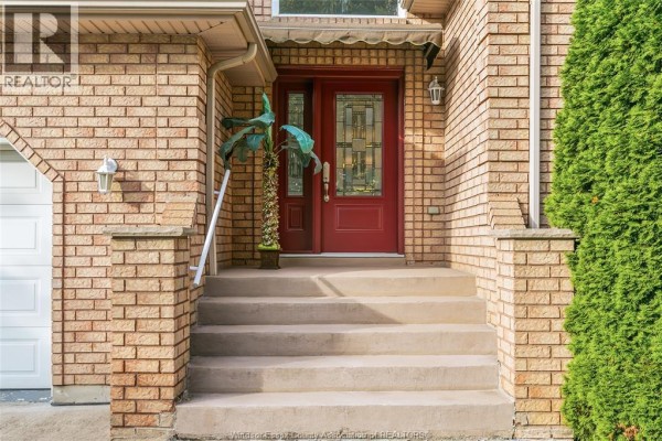 Front entrance of a brick house with concrete steps and a red door. - 445 John Harvey Crescent, Windsor