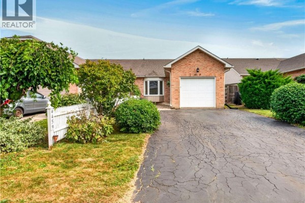 View of the brick townhouse exterior with a driveway, lawn, and mature landscaping. - 4459 Christopher Court, Beamsville