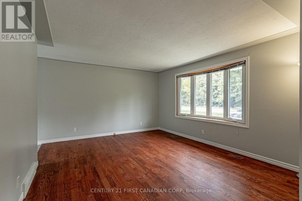 Spacious living room with hardwood floors and a large window overlooking greenery. - 4459 Hamilton Road, Thames Centre