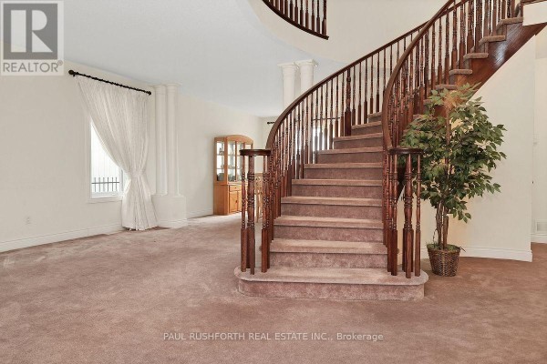 Spacious living area with a curved wooden staircase, carpeted floor, and large windows. - 446 Frank Cauley Way, Ottawa