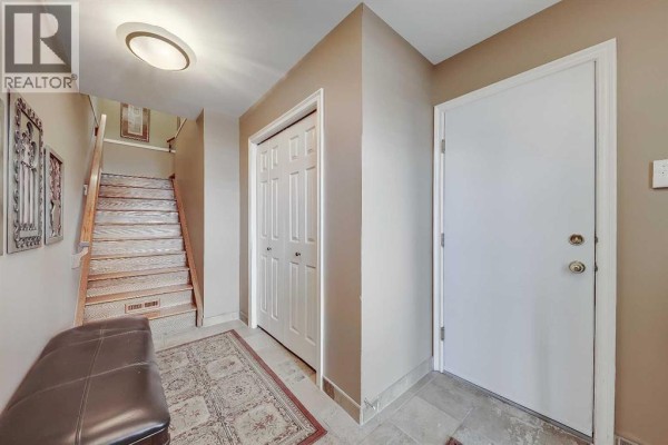 Foyer with cream walls, tile floor, and wood staircase leading upwards. - 446 Killarney Glen Court Sw, Calgary