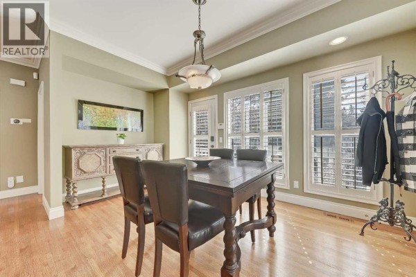 Bright dining area with a wooden table, leather chairs, and large windows with shutters. - 446 Killarney Glen Court Sw, Calgary