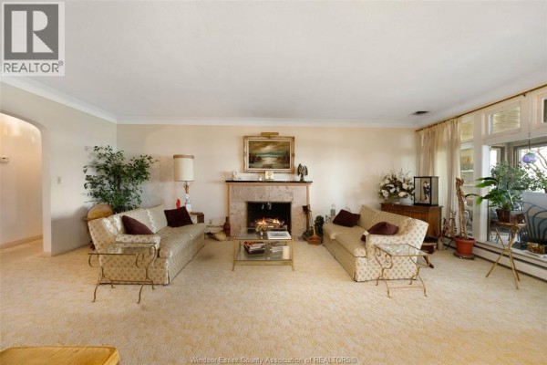 Living room with a fireplace, two patterned sofas, and a large carpeted area. - 4470 Riverside Drive, Windsor