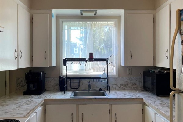 U-shaped kitchen with white cabinets, a double sink, and a window with sheer curtains. - 4475 Byng Rd, Port Hardy