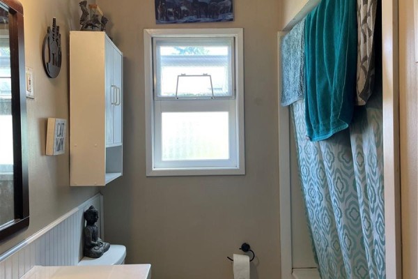 Bathroom with a toilet, a white cabinet, a window, and a teal patterned shower curtain. - 4475 Byng Rd, Port Hardy
