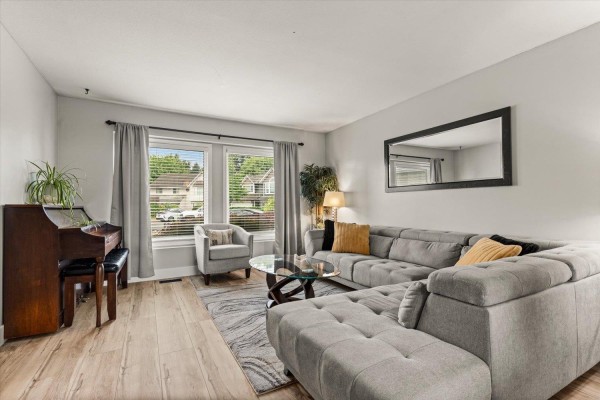 Living room with a large sectional sofa, armchair, glass coffee table, piano, and a large mirror. - 44756 Lancaster Drive, Sardis South, Chilliwack