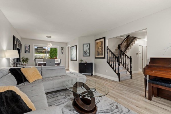Living room with sectional sofa, piano, dining area, and stairs leading to the upper floor. - 44756 Lancaster Drive, Sardis South, Chilliwack