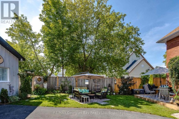 Green backyard with a wooden fence, outdoor furniture, and umbrellas. - 449 Elizabeth Street, Midland