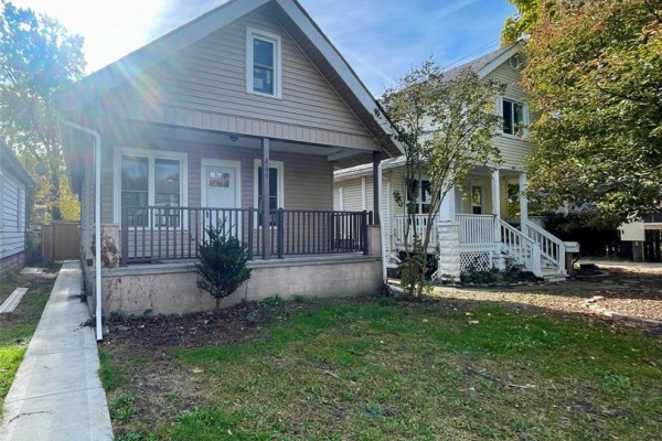 Side view of a beige-sided house with a covered porch and a concrete foundation. - 449 Ellis Street West, Windsor