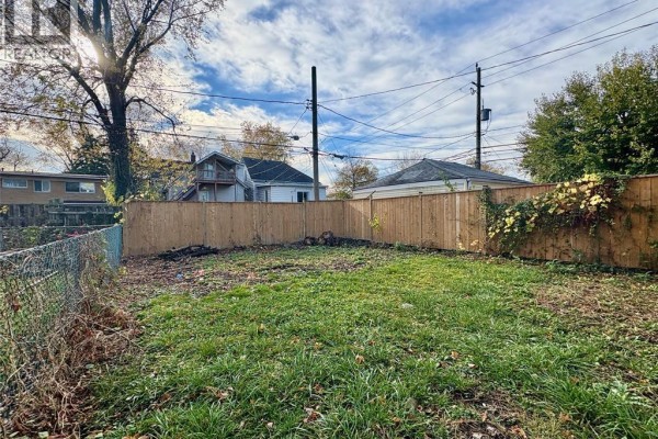 Backyard with a chain-link fence, wooden fence, and grassy lawn. - 449 Ellis Street West, Windsor