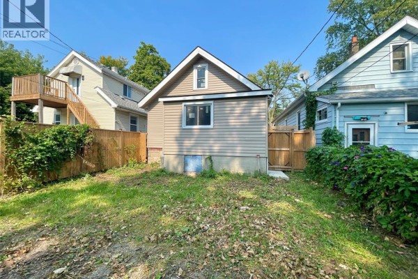 Rear exterior of a beige-sided house with a small window and a concrete foundation. - 449 Ellis Street West, Windsor
