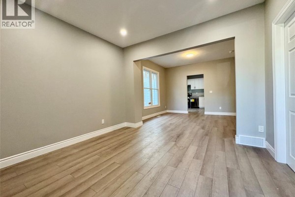Living room with beige walls, light wood laminate flooring, and an archway to the kitchen. - 449 Ellis Street West, Windsor