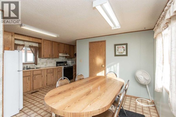 Kitchen and dining area with wood cabinets, checkered floor, wood dining table with four chairs, and white appliances. - 44a, 5500 Womacks Road, Blackfalds