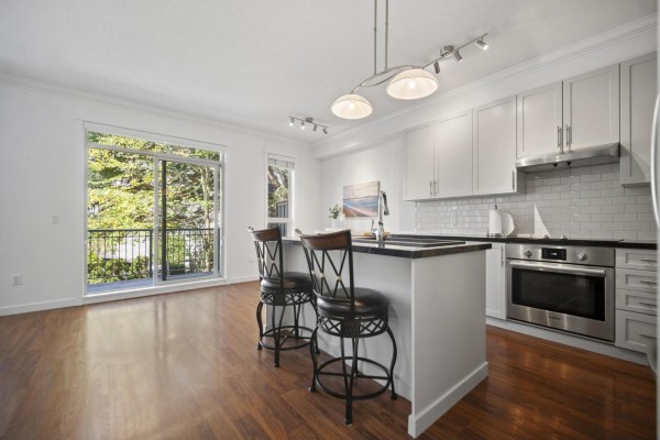 Kitchen with white cabinets, stainless steel appliances, and island with two bar stools overlooking a balcony. - 45 2738 158 Street, Surrey