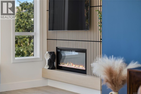Close-up of a modern electric fireplace with a decorative surround and a window with white curtains. - 45 368 Tradewinds Ave, Colwood