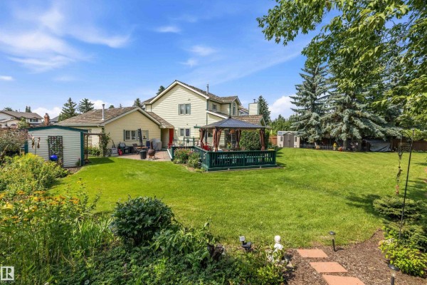 Backyard view of the house, featuring a deck with a gazebo and a sprawling green lawn. - 45 Blue Quill Cr Nw, Edmonton
