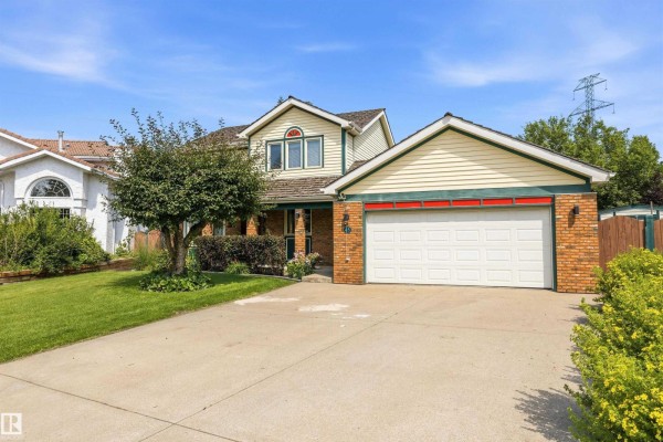 A concrete driveway leads to the entrance of a house with a brick and light yellow exterior. - 45 Blue Quill Cr Nw, Edmonton