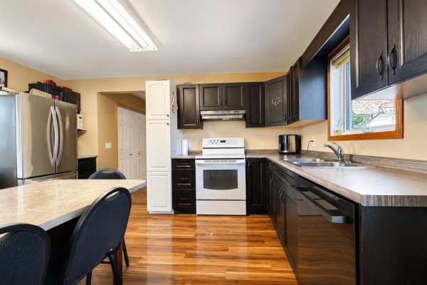 U-shaped kitchen with dark wood cabinets, white oven, stainless steel sink, and dining area. - 45 Bredin Avenue, Rosenfeld