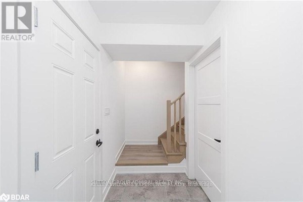 Entrance hallway with white doors, grey tiled floor, and a wooden staircase to the right. - 45 Hay Lane, Barrie