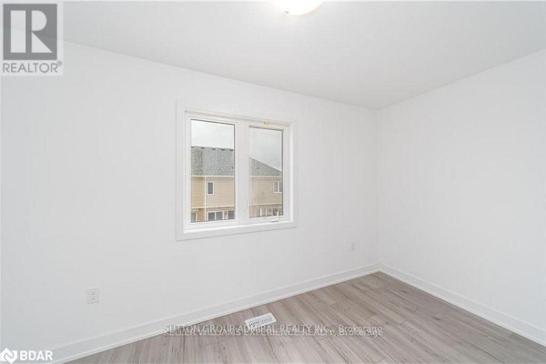 Interior room with white walls, light wood laminate flooring, and a window facing other townhouses. - 45 Hay Lane, Barrie