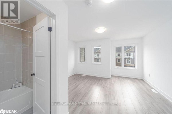 Bedroom with white walls, light wood laminate flooring, multiple windows, and an open bathroom door on the left. - 45 Hay Lane, Barrie