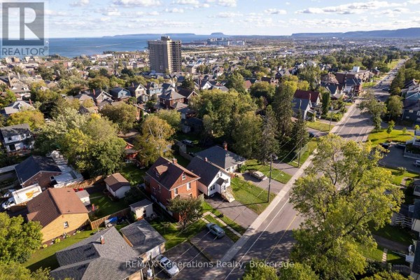 Aerial view of a neighborhood with houses, trees, and distant city buildings by the water. - 45 High Street N, Thunder Bay