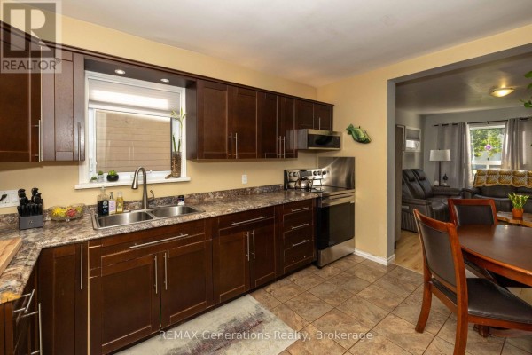 Kitchen with dark wood cabinets, granite countertops, stainless steel appliances, and a dining table. - 45 High Street N, Thunder Bay