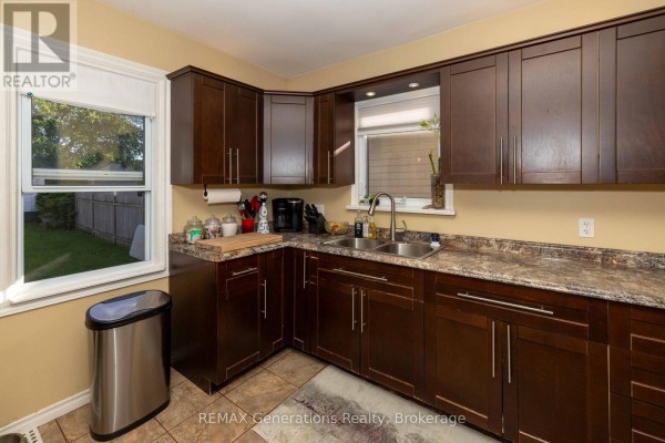 Kitchen with dark wood cabinets, granite countertops, double sink, and view of the backyard. - 45 High Street N, Thunder Bay