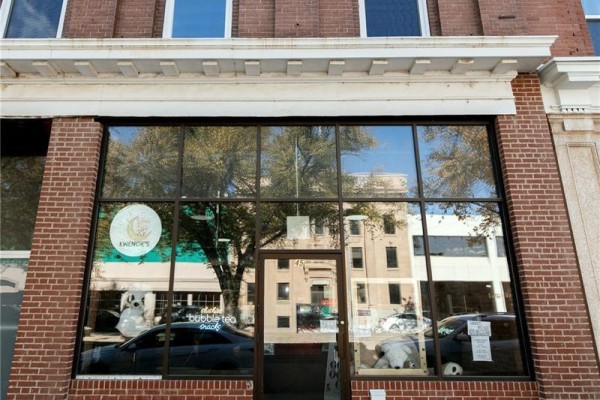 A storefront with large windows displaying "Kwencie's" logo and interior decor, reflecting street. - 45 High Street W, Moose Jaw